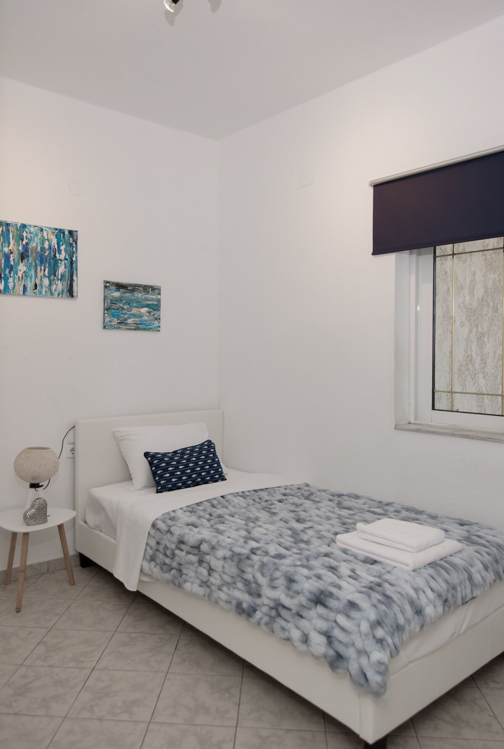 Un dormitorio con cama, una mesita, lámpara y cuadros en la pared.