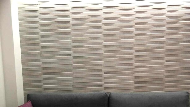 Une pièce avec un canapé gris, un mur à motifs et un coussin blanc.