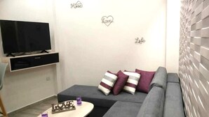 Olohuone, jossa on litteänäyttöinen televisio, sohva, sohvapöytä ja koristeellisia taideteoksia seinillä.
