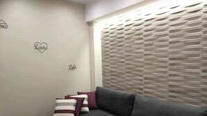 Un salon moderne avec un canapé gris, des coussins à rayures, une petite table d’appoint et un mur orné d’un décor en forme de cœur.