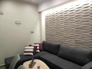 Een moderne woonkamer met een grijze bank, gestreepte kussens, een klein bijzettafeltje en een muur met een decoratie in de vorm van een hart.
