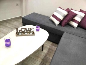Un salon moderne avec une table basse blanche, un canapé gris agrémenté de coussins à rayures et un panneau décoratif sur lequel on peut lire le mot « AMOUR ».