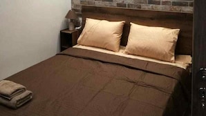 Une chambre à coucher avec une tête de lit ornée d’un motif en briques, un lit avec une literie beige et une table de chevet avec une lampe.