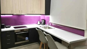 Kompakti keittiö, jossa on valkoinen työtaso, sisäänrakennettu uuni, pesuallas ja violetti välitilan laatoitus.