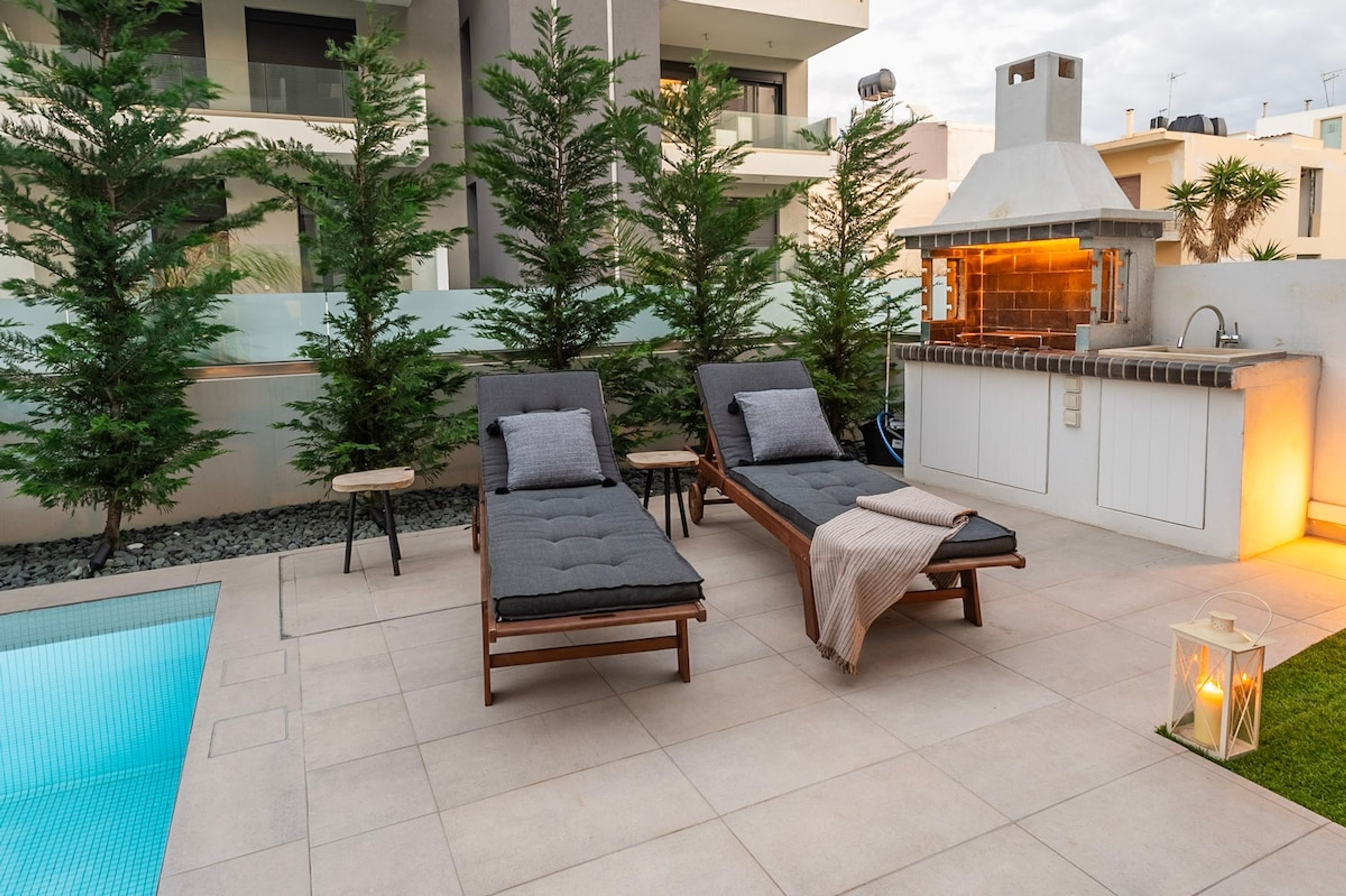 A poolside area with two lounge chairs, a small table, a barbecue grill, and a pool.