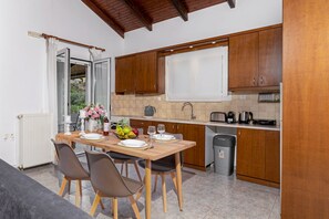A compact kitchen with wooden cabinets, a dining table with chairs, a window with curtains, and a view of greenery outside. - Elva Luxury Villa With Private Pool (Hersonissos)