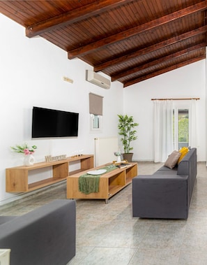A modern living room with a wooden ceiling, a flat-screen TV, a sofa, a coffee table, and a potted plant. - Elva Luxury Villa With Private Pool (Hersonissos)