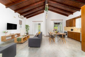 A spacious living area with a high ceiling, a sofa, a dining table with chairs, and a kitchen area with wooden cabinets. - Elva Luxury Villa With Private Pool (Hersonissos)