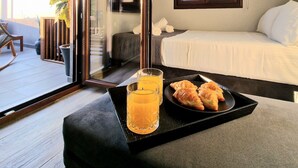 A hotel room with a bed, a bedside table with a tray of croissants and orange juice, a TV, and a window with a view of the outside. - D A Luxury Suite Jacuzzi (Malevizi)