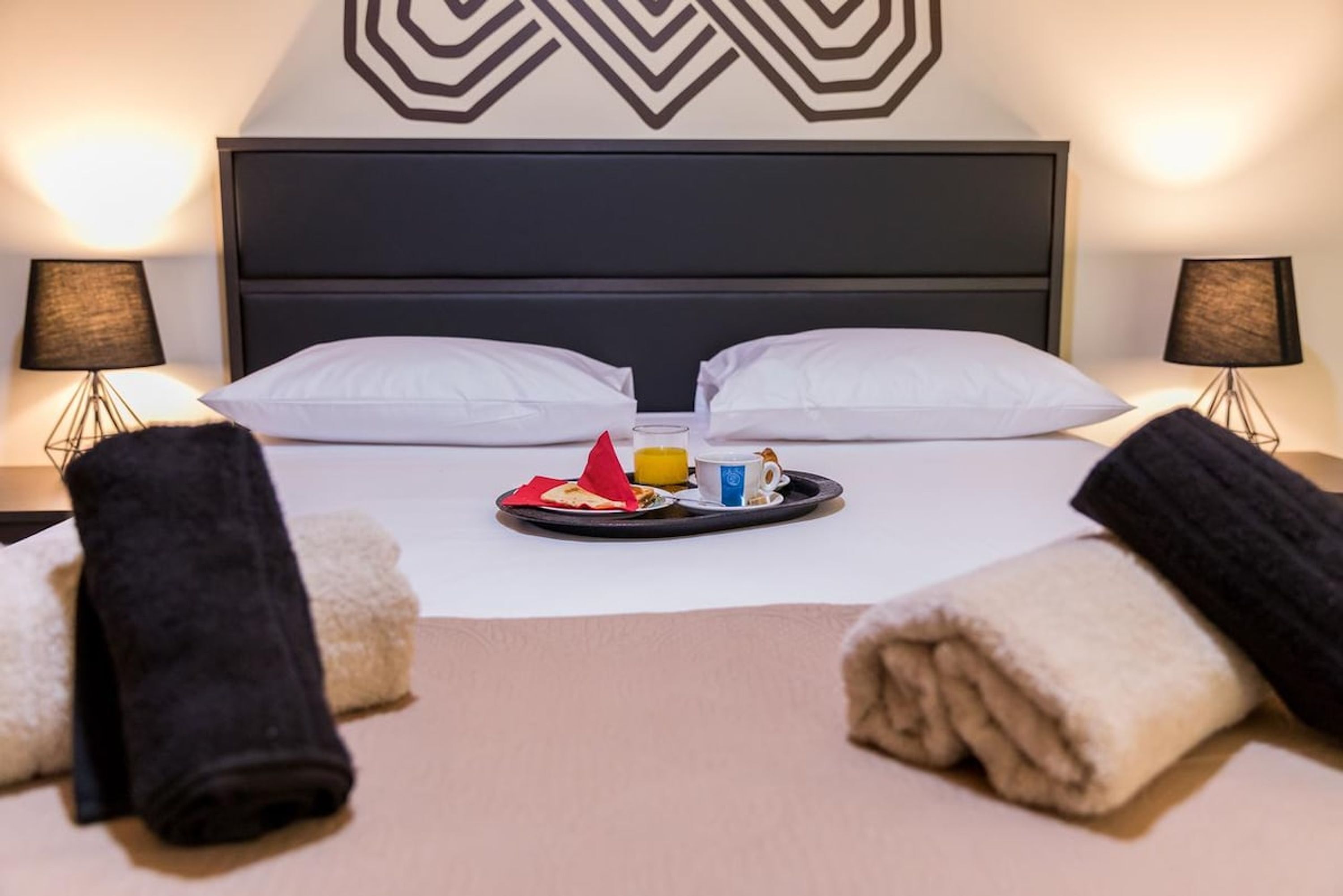 A hotel room with a bed, pillows, a tray with breakfast items, and towels.