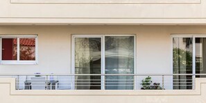 Une façade d’immeuble avec de grandes fenêtres, un balcon doté d’une balustrade et une petite table avec des chaises.