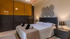 Moderni hotellihuone, jossa on suuri sänky, yöpöydät ja geometrisesti kuvioitu seinätaideteos.