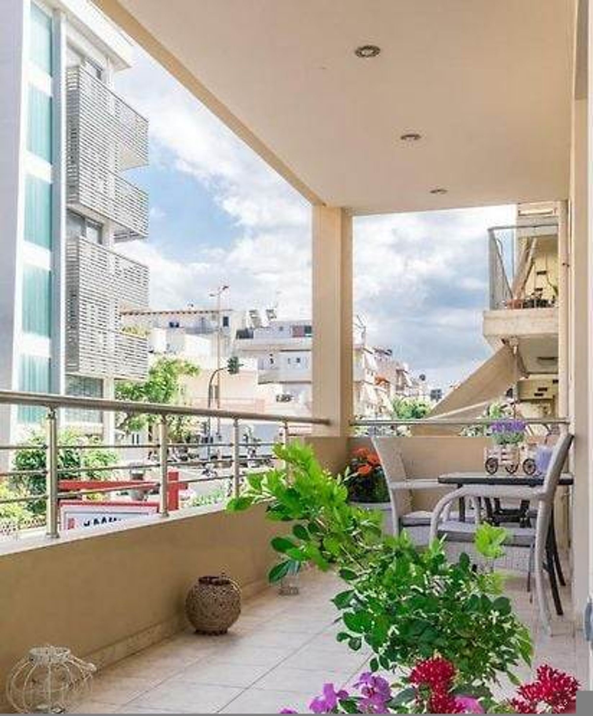 A balcony with a view of buildings, a potted plant, and a table with chairs.
