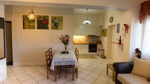 Un coin repas avec une table dressée pour deux personnes, un canapé et une cuisine en arrière-plan.