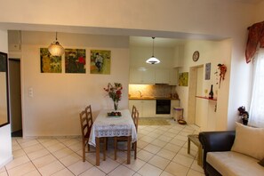 A dining area with a table set for two, a sofa, and a kitchen in the background. - Kostas Apartment Very Near to Amoudara Beach (Malevizi)