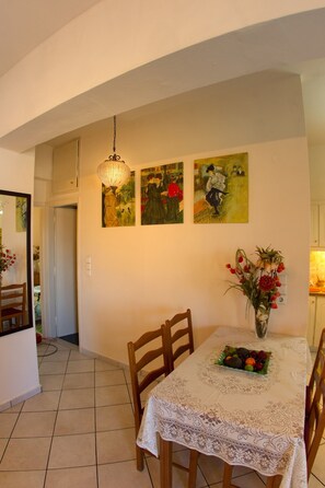 A dining area with a table set for four, chairs, a vase with flowers, and wall art. - Kostas Apartment Very Near to Amoudara Beach (Malevizi)