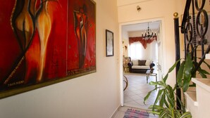 Un couloir orné d’un grand tableau abstrait, un escalier et un salon avec un canapé et un lustre.