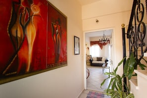 A hallway with a large abstract painting, a staircase, and a living room with a sofa and a chandelier. - Kostas Apartment Very Near to Amoudara Beach (Malevizi)
