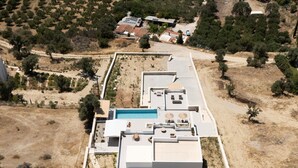 Una vista aerea di un edificio moderno con piscina, immerso in vegetazione arida e qualche albero.