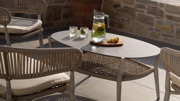 Un patio con sedie in vimini, un tavolino rotondo, una brocca d'acqua con fette di limone e una pianta in vaso.