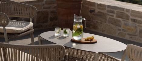 A patio with wicker chairs, a round table, a pitcher of water with lemon slices, and a potted plant.