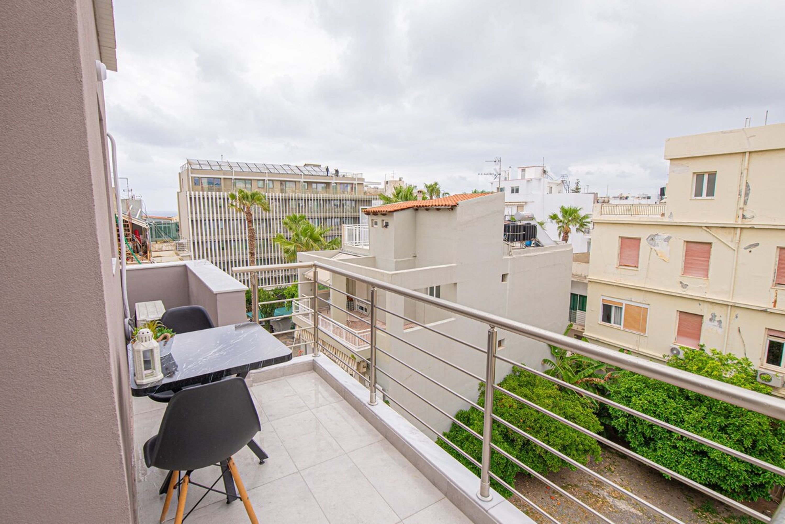 A balcony with a table and chairs, a railing, and a view of surrounding buildings.