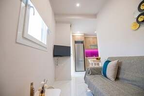 A compact living space with a sofa, a flat-screen TV, a kitchen area with a fridge, and a dining table. - Aretousa Apart Heraklion City (Heraklion)