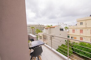 A balcony with a table and chairs, a railing, and a view of neighboring buildings and greenery. - Aretousa Apart Heraklion City (Heraklion)