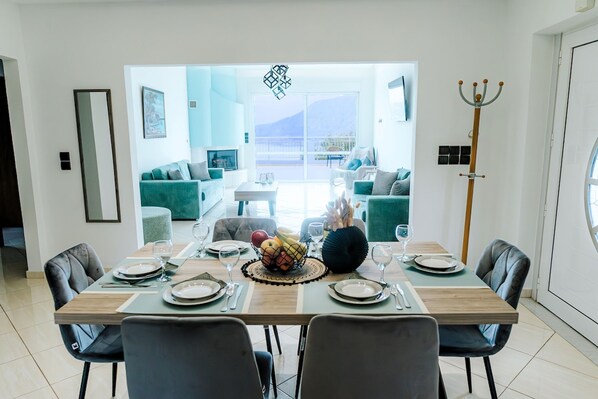Un coin repas avec une table dressée pour six personnes, un panier de fruits et une vue sur un balcon aménagé avec des sièges d’extérieur.