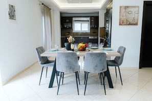 A dining area with a table set for four, chairs, a vase with flowers, and a fruit bowl. - Aithra House With Beautiful View (Chania)
