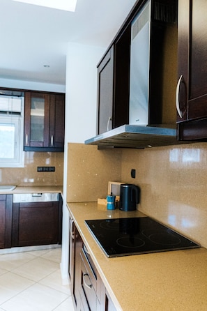 A modern kitchen with dark wooden cabinets, a stainless steel range hood, and a black induction cooktop. - Aithra House With Beautiful View (Chania)