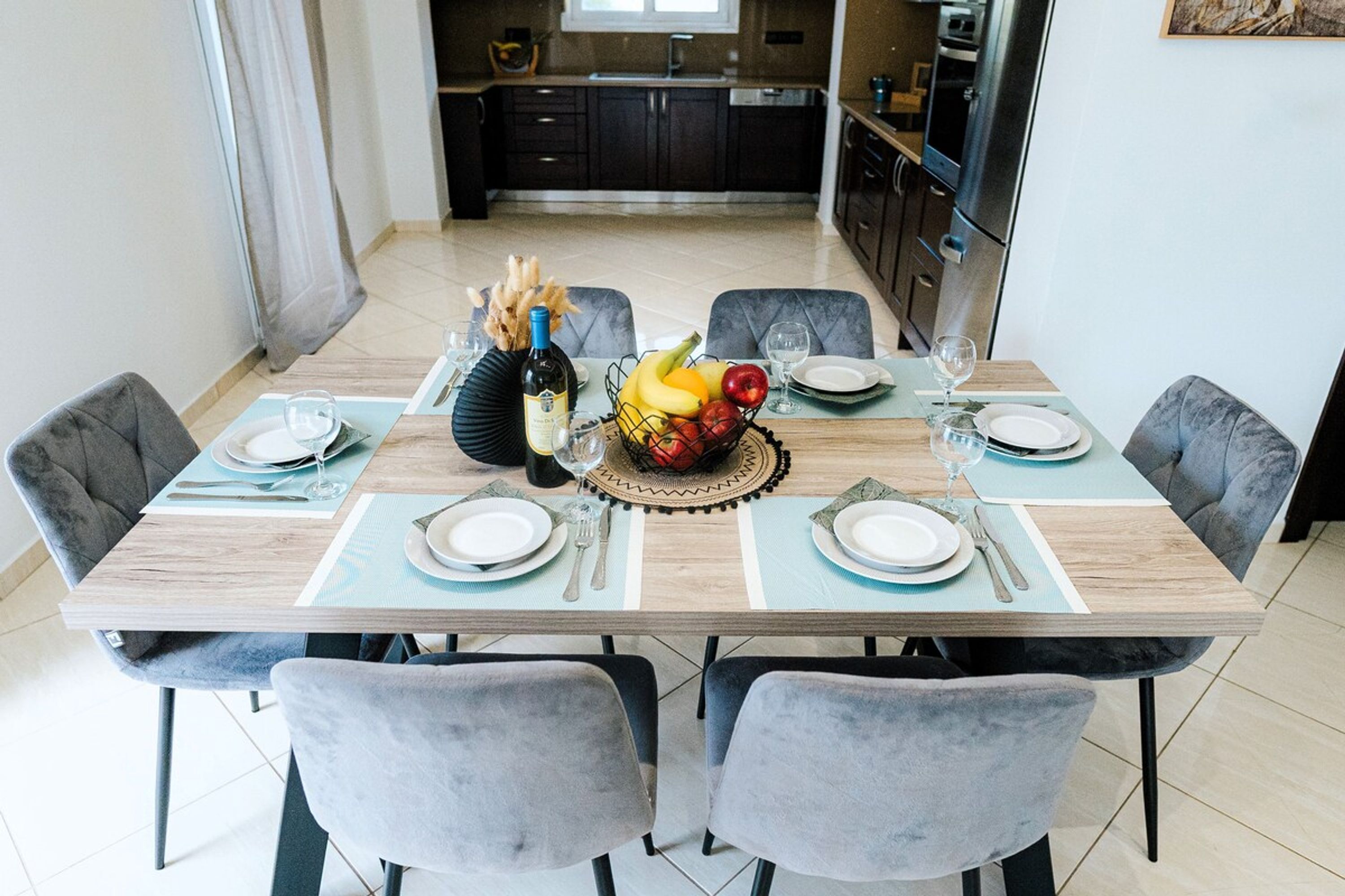 A dining table set with plates, cutlery, a fruit bowl, and a bottle of wine.