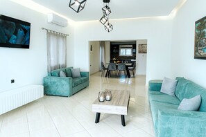 Un salon moderne avec des canapés de couleur turquoise, une table basse en bois et un coin repas à l’arrière-plan.