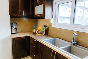 A kitchen with dark wood cabinets, a double sink, a window, and a fruit bowl on the counter. - Aithra House With Beautiful View (Chania)