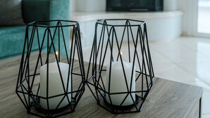 Zwei geometrische Kerzenständer auf einem Holztisch, im Hintergrund ein Türkis-farbenes Sofa und ein Kamin.