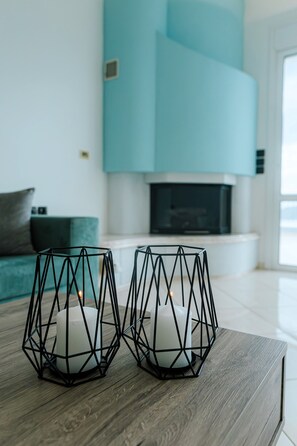 Deux chandeliers aux formes géométriques sont posés sur une table en bois, devant un canapé turquoise et surmontés d’une cheminée en arrière-plan.