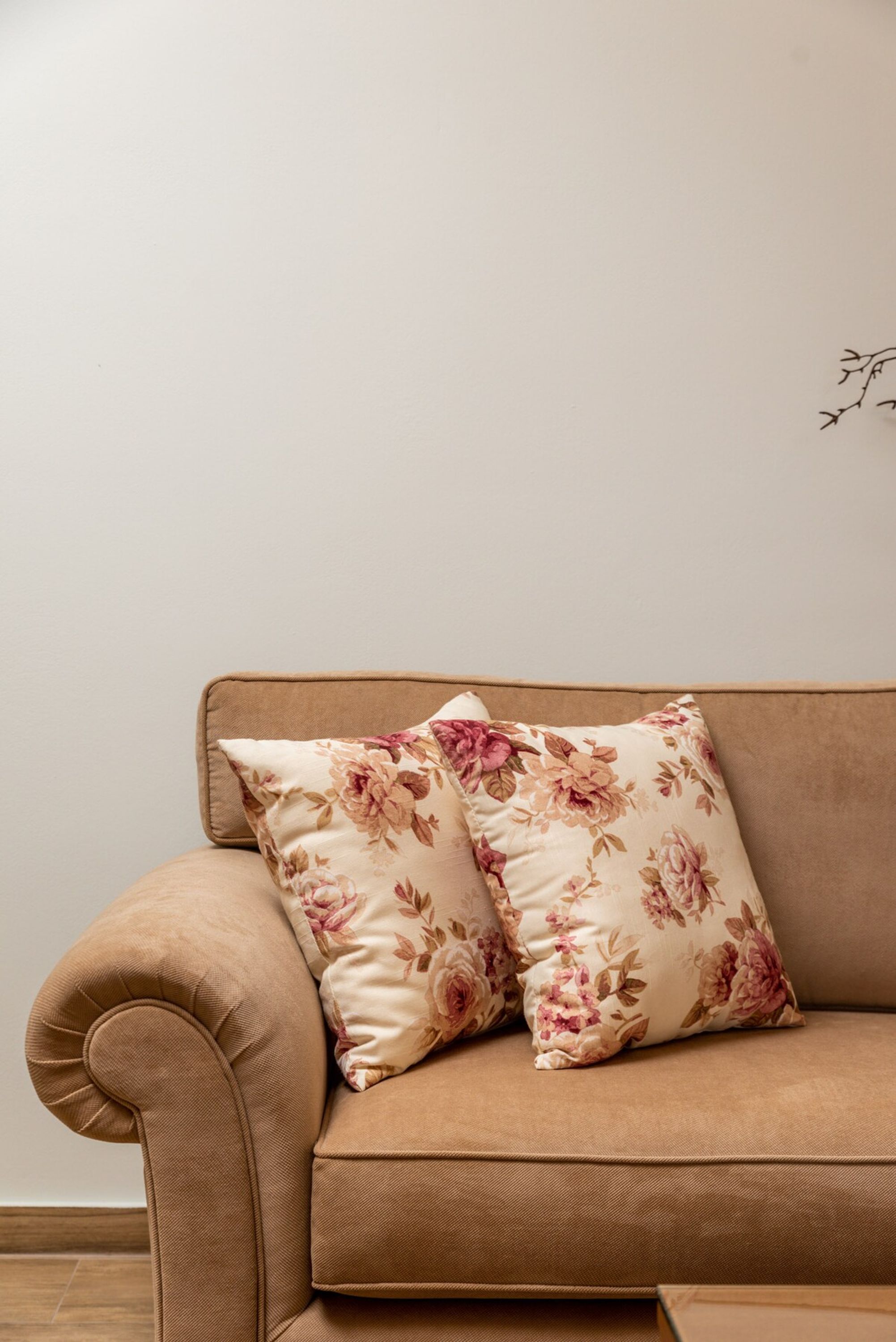 A beige sofa with floral cushions against a plain wall.