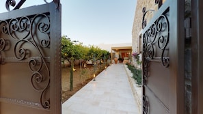 A gated entrance with a pathway leading to a building, surrounded by a landscaped garden with plants and a small tree. - Cretan Rhapsody Villa With Private Yard (Faistos)