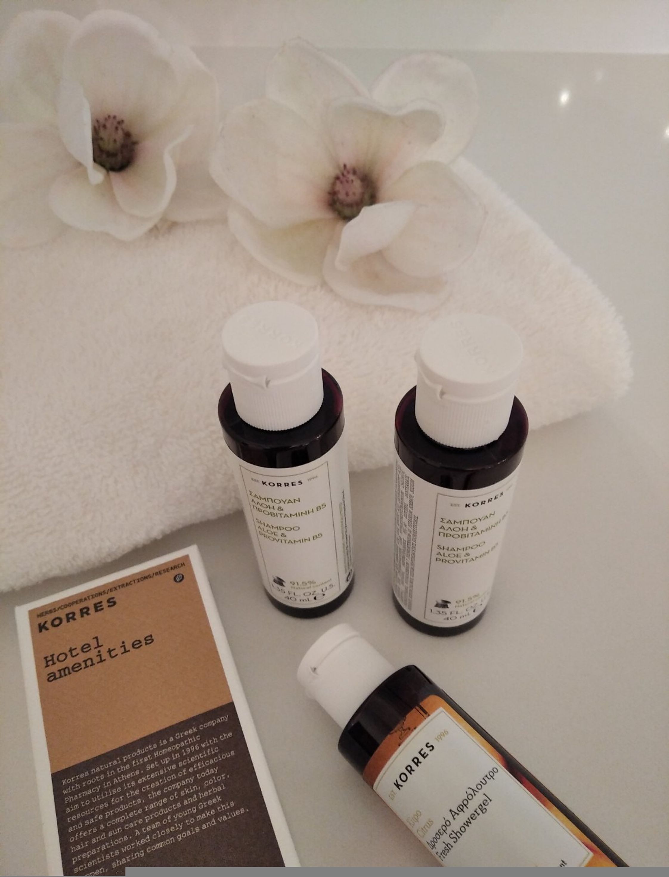 Two Korres shampoo bottles and a Korres shower gel on a white surface with a brochure.