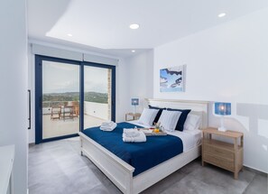 Een moderne slaapkamer met een bed, nachtkastjes, uitzicht door een schuifdeur op een buitenruimte en een schilderij aan de muur.