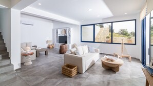 A modern living room with a sofa, coffee table, and a large window with a view of a stone staircase. - Kyma Luxury Villa With Private Pool (Faistos)