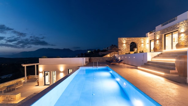A modern pool area with a stone wall, outdoor seating, and a view of the mountains. - Kyma Luxury Villa With Private Pool (Faistos)