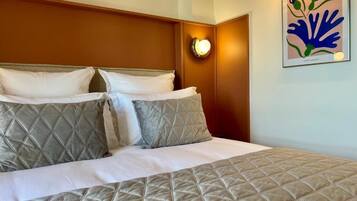 Habitación de hotel con cama, almohadas, luz empotrada en la pared y una obra de arte enmarcada.