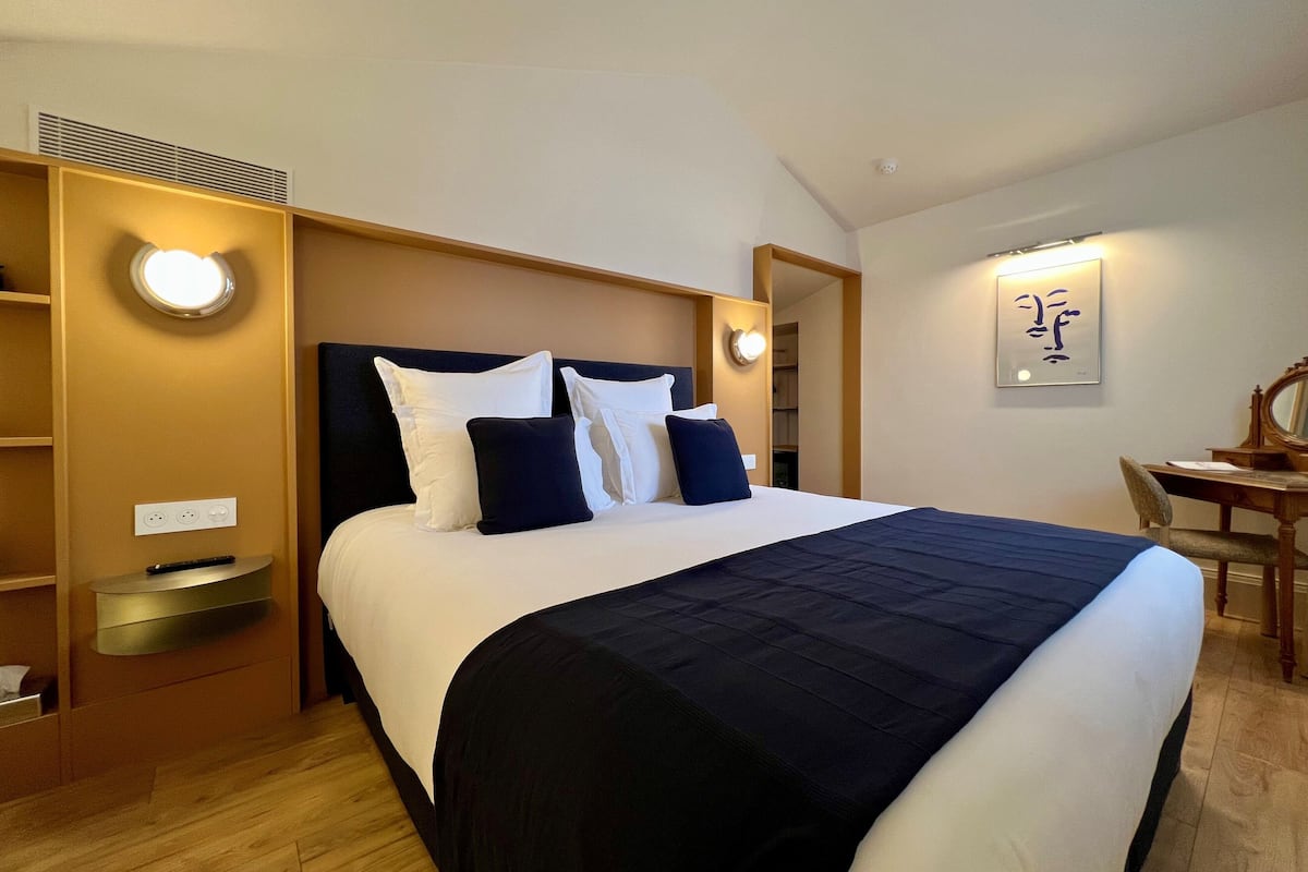 A hotel room with a large bed, bedside lamps, a desk with a chair, and a wall-mounted artwork.