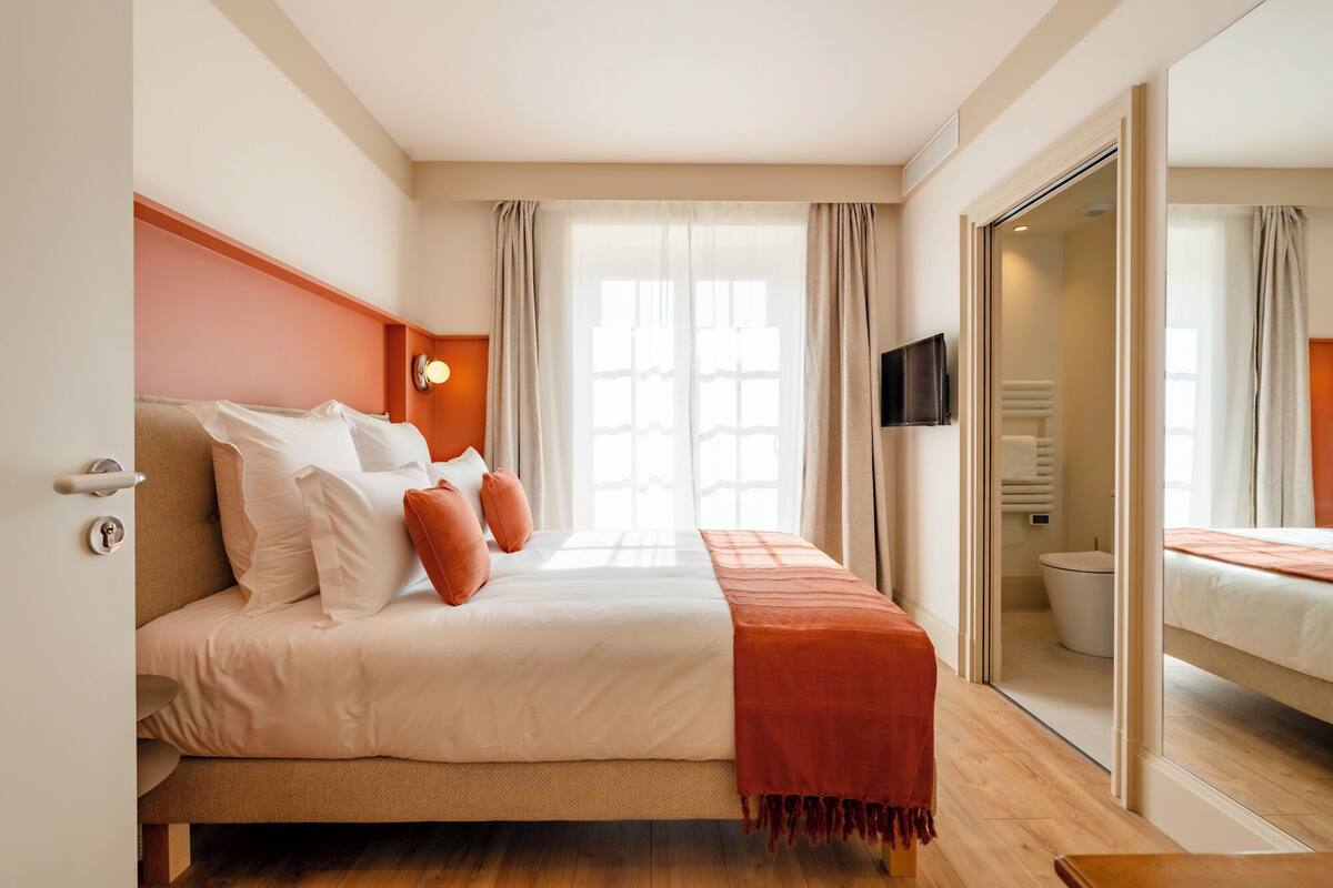 A hotel room with a bed, a television, a window with curtains, and a view of the bathroom.