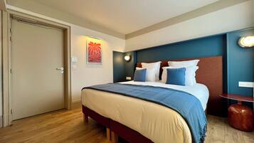 A hotel room with a bed, a door, a wall-mounted light, and a small table.