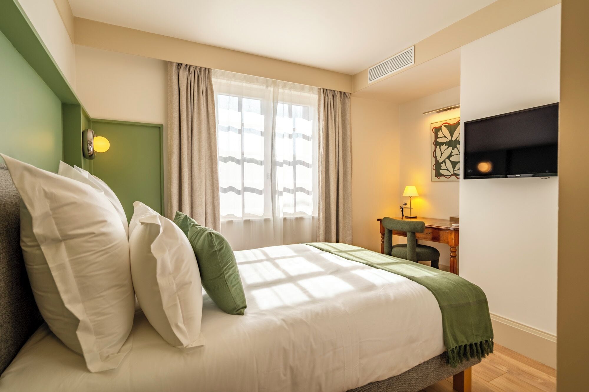Ein Hotelzimmer mit Bett, Schreibtisch, Stuhl, Fernseher und einem fensterbelagten Fenster.