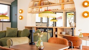 A modern dining area with a wooden table, orange cushioned chairs, and a green sofa. - Hôtel Villa Maitia (Ustaritz)