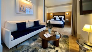 A hotel room with a bed, a sofa, a coffee table, a TV, and a wall-mounted artwork. - Hôtel Villa Maitia (Ustaritz)