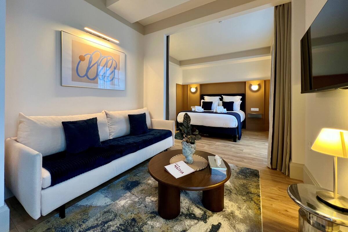 A hotel room with a bed, a sofa, a coffee table, a TV, and a wall-mounted artwork.